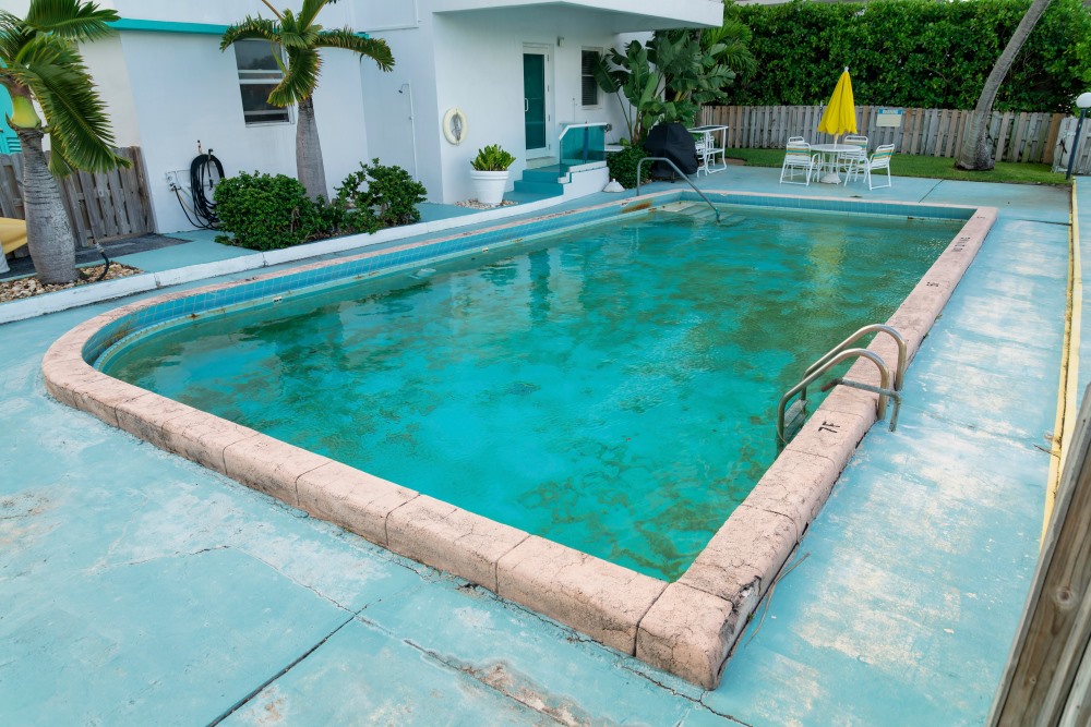 An image of an older pool with structural issues in a backyard.